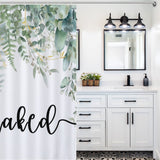 Bathroom with a white vanity, black-framed mirror, and a leafy Cotton Cat shower curtain featuring the words "Get Naked." The eucalyptus leaves print on the Get Naked Funny Letters Eucalyptus Leaves Print Shower Curtain-Cottoncat adds a touch of nature to the elegant bathroom decor.