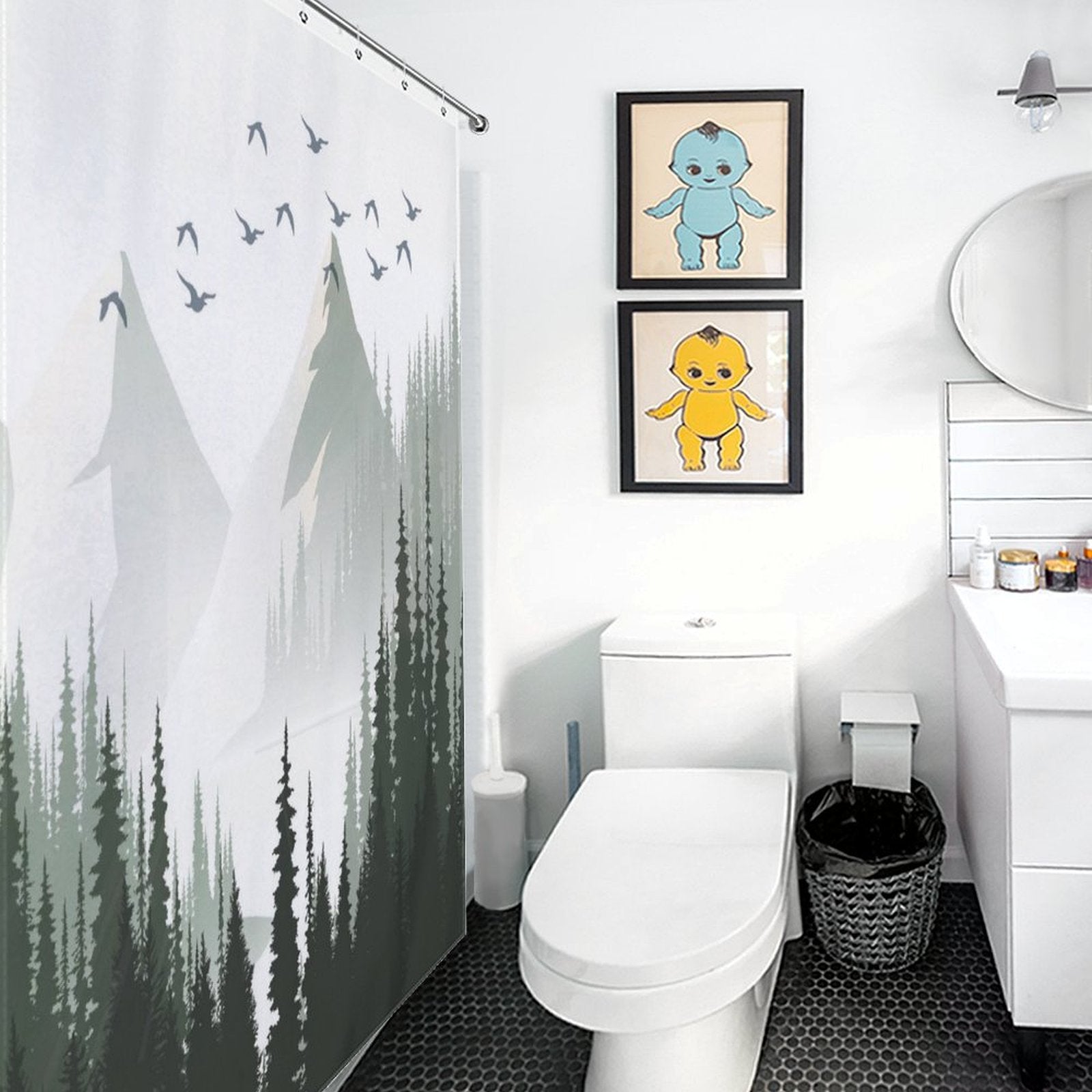 A modern bathroom with a Green Misty Forest Shower Curtain Ombre Sage Green White Nature Tree Mountain Woodland-Cottoncat by Cotton Cat, two framed pictures of cartoon characters above the toilet, white vanity, mirror, and black hexagonal floor tiles. This tranquil bathroom decor creates a serene ambiance perfect for unwinding.