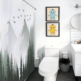 A modern bathroom with a Green Misty Forest Shower Curtain Ombre Sage Green White Nature Tree Mountain Woodland-Cottoncat by Cotton Cat, two framed pictures of cartoon characters above the toilet, white vanity, mirror, and black hexagonal floor tiles. This tranquil bathroom decor creates a serene ambiance perfect for unwinding.