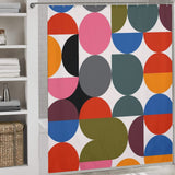 Abstract Modern Art Rainbow Polka Dot Geometric Shower Curtain-Cottoncat by Cotton Cat with a geometric pattern featuring large colorful circles and semi-circles in red, blue, pink, orange, green, and black, creating an abstract modern art feel. White shelving with towels and baskets is visible to the left.