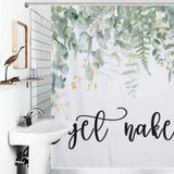 Bathroom with a white sink and a nature-themed shower curtain featuring eucalyptus leaves prints and the phrase "Get Naked" in cursive writing. A wooden bird sculpture is placed on a shelf beside the mirror.