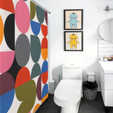 Bathroom with a Cotton Cat Abstract Modern Art Rainbow Polka Dot Geometric Shower Curtain. The room includes a white toilet, black trash bin, and two framed cartoon prints above the toilet, adding a touch of abstract modern art.