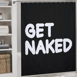 A Funny Black and White Letters Get Naked Shower Curtain-Cottoncat by Cotton Cat with the bold phrase "GET NAKED" in large white letters. Shelving with folded towels and a woven basket is visible to the side, adding a touch of humor to your bathroom decor.