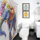 Bathroom with a vibrant, Cotton Cat Artistic Painting Happy Elephant Shower Curtain-Cottoncat, framed pictures of cartoon characters on the wall, a toilet, a black wastebasket, and a white sink with a round mirror above it.