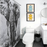 Modern bathroom with an elegant Black and White Elephant Shower Curtain-Cottoncat by Cotton Cat, two framed child-like drawings, a round mirror, a white toilet, sink, trash bin, and dark hexagonal floor tiles. Ideal for those who appreciate stylish bathroom decor.