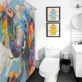 A bathroom with a toilet, sink, and a delightful Cute Happy Elephant Shower Curtain-Cottoncat by Cotton Cat. Two framed prints of cartoon characters are on the wall, adding to the playful vibe. The floor features dark hexagonal tiles.