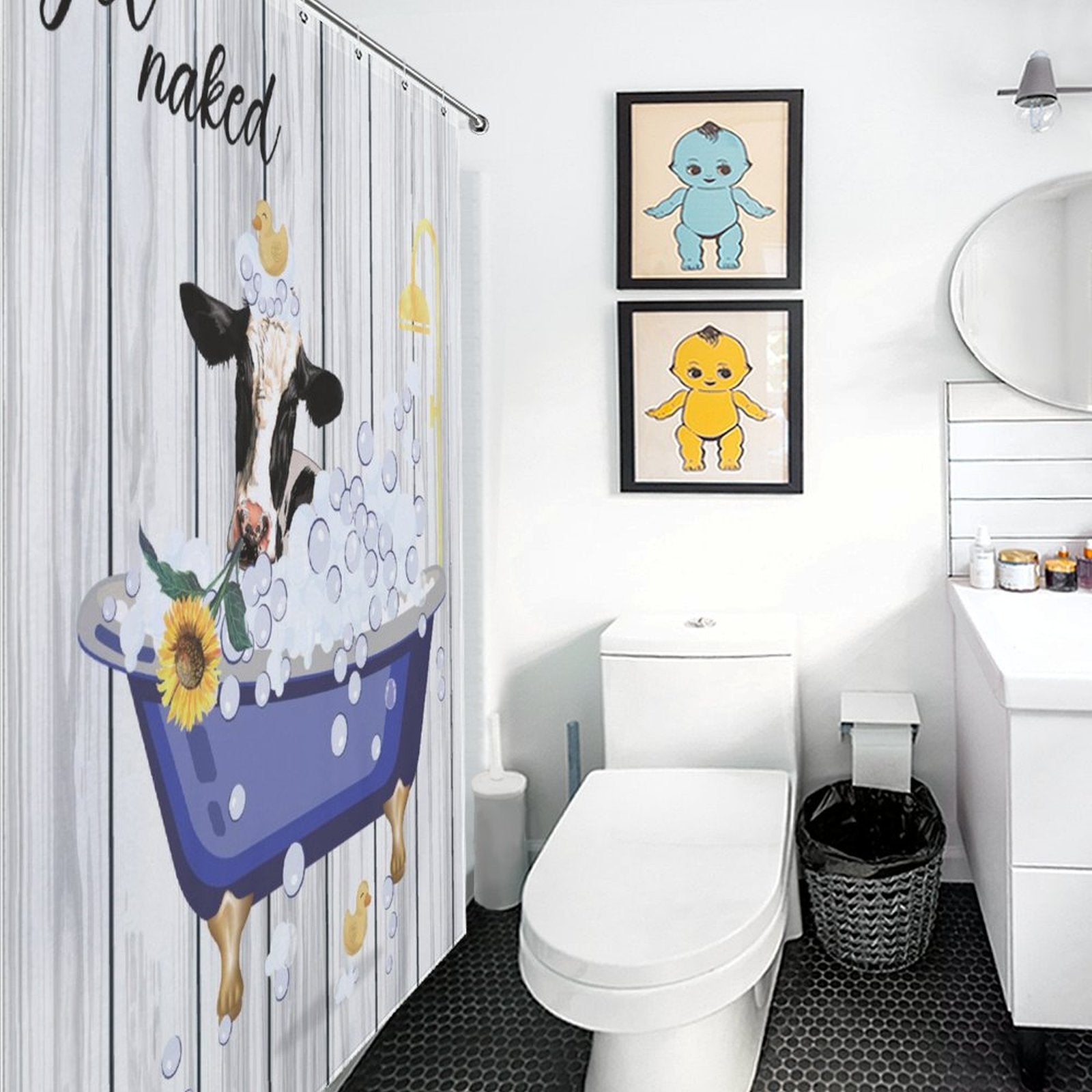 A bathroom with a Funny Cow Sunflowers Get Naked Shower Curtain-Cottoncat, two framed prints above the toilet, a circular mirror, a sink, and a wastebasket. The floor is covered with black hexagon tiles.
