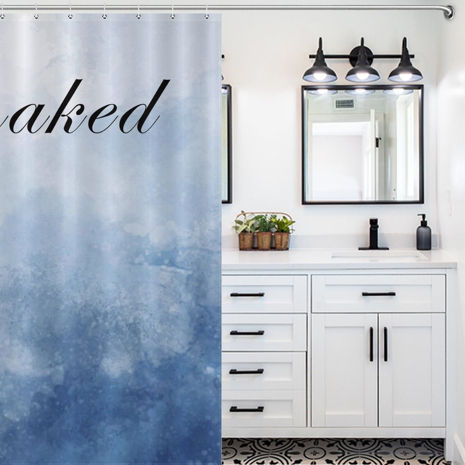 A bathroom with white cabinets, black hardware, a sink, and a large mirror with three lights above. A Funny Letters Abstract Blue Get Naked Shower Curtain-Cottoncat by Cotton Cat is partially visible on the left, adding a playful touch with its text in bold letters.