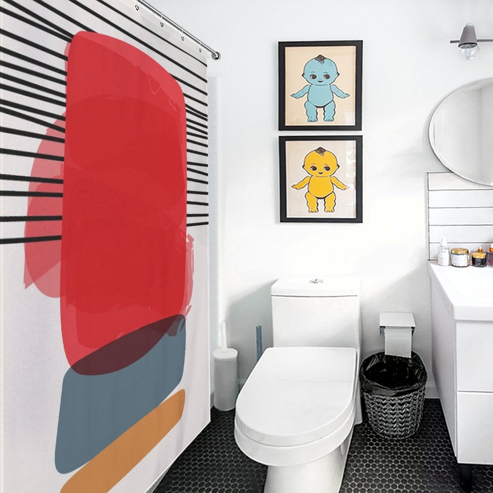 A modern bathroom with a white toilet, a round mirror above a sink, and a black trash bin. The Cotton Cat shower curtain features bold abstract art that seamlessly blends with the modern geometric art theme. Two framed artworks of cartoon characters adorn the wall, adding a whimsical touch to the decor.