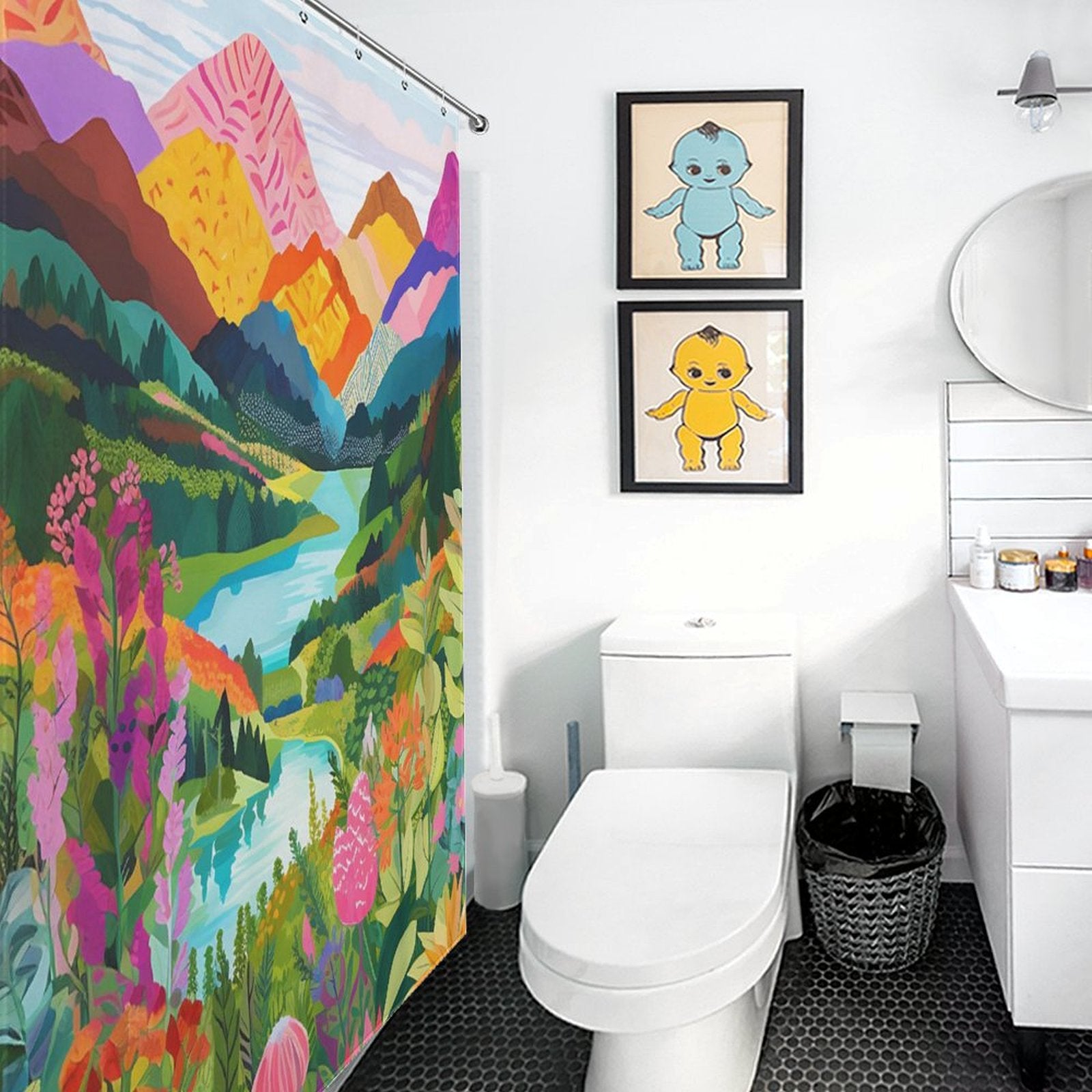 A bright bathroom featuring a Cotton Cat Nature Forest Lake Watercolor Art Painting Landscape Colorful Green Mountain Abstract Shower Curtain, a toilet, a vanity with a circular mirror, and two framed cartoon pictures of blue and yellow characters on the wall. The nature-inspired decor adds a charming touch.