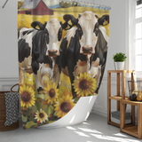 A Farmhouse Black White Cow Sunflower Shower Curtain from Cotton Cat, featuring two black and white cows standing among sunflowers with a red barn in the background. The bathroom decor includes a wicker basket and a wooden shelf with a potted plant.